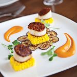Page-3-and-4_Rusty-Pelican—Pan-Seared-Day-Boat-Sea-Scallops—saffron-risotto-cakes,-sweet-eggplant,-roasted-red-pepper-coulis.-Photo-credit-Michael-Pisarri
