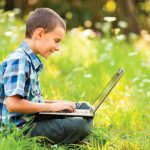 Palmer-Trinity_10452847-school-boy-using-his-laptop-outdoor-on-a-meadow