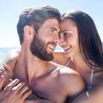 Happy couple hugging and smiling at each other at the beach