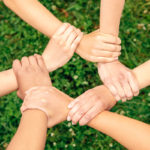 Volunteering. Young people volunteers outdoors together holding hands unity top view close-up