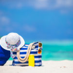 Blue stripe bag and towel, straw white hat, sunglasses, sunscreen bottle on exotic beach