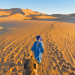 14400688 – berber walking with camel at erg chebbi orange dunes, morocco