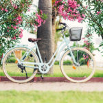 Women vintage bicycle against green bushes and pink flowers. Stylish retro bicycle with the basket parked on the street.