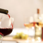 Pouring red wine from bottle into glass on blurred background. S
