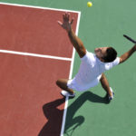 young man play tennis outdoor on orange tennis court at early morning