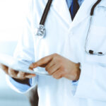 Doctor man using tablet computer for network research or virtual disease treatment, hands close-up. Perfect medical service in clinic. Modern medicine, medic data and healthcare concepts. Toned picture