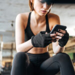 Woman athlete sitting and using smartphone in gym