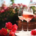 Pouring wine into glass on table in blooming rose garden. Space